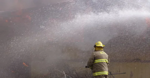 Slow-motion view of a fireman with a hose walking toward a burning house while Stock Footage 59222754