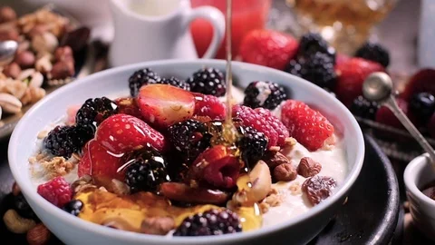 Slow motion view: pouring honey over a bowl of cereals with berries Stock Footage 74066369