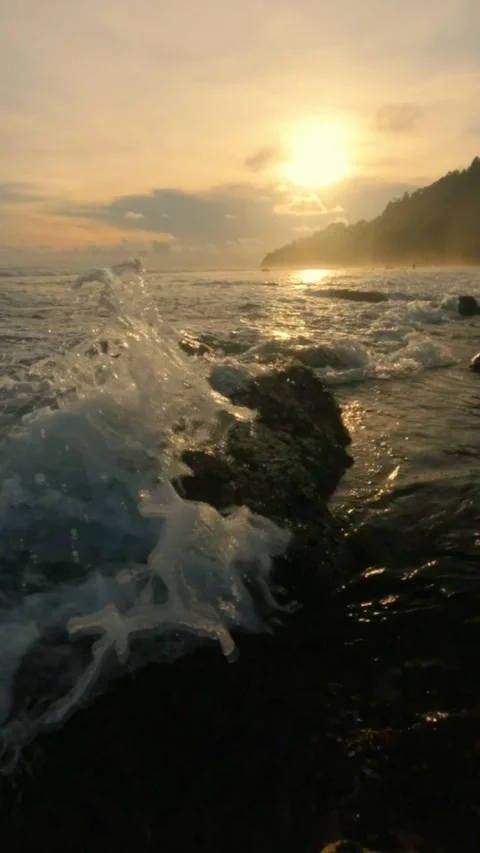 Slow motion view of waves crashing against the rocks on the beach at sunset Stock Footage 319921745