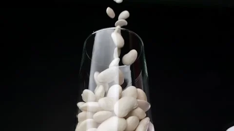 Slow-motion visual of white beans going into glass storage, against a black.. Video stock 262527987