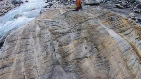 Slow motion of walking up to brown boulder of rock with pile of gravel near a ri Stock Footage 265493400