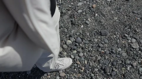 Slow motion walking on rocky ground in white sneakers and pants Stock Footage 312374077