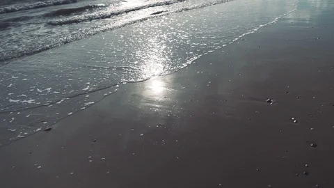Slow motion walking shot as waves lap sandy beach with sun reflection v2 Stock Footage 119534049