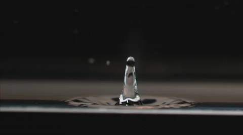 Slow motion, water droplet falls to calm surface, splashing on black Stock Footage