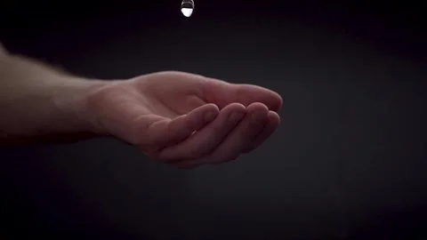 Slow motion water droplets falling in open caucasian hand on black Stock Footage 250251078