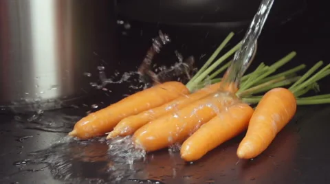 SLOW MOTION: Water stream falls on a carrots on a table in a kitchen Видео 68155851
