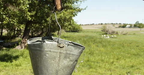 Slow motion. Water washes over an old bent bucket rising from a well. Stock Footage 141789709