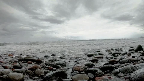 Slow motion wave crashes over stony beach into camera on stormy afternoon Stock Footage 98426136
