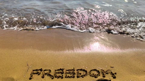 Slow motion wave erasing freedom text on beach Video stock 335758392