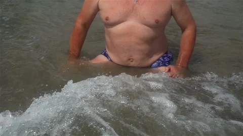 Slow motion of a wave running on a man sitting in the water Stock Footage 114301265