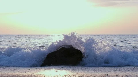 Slow motion wave splashing over rock on beach at sunset. Low angle. Stock Footage 115999935