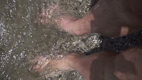 Slow motion wave washes and splashes about man's legs standing Stock Footage 112935458
