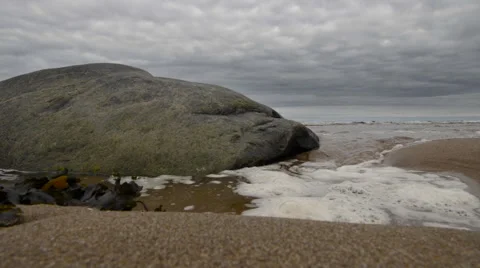 Slow Motion - Wave washing up beach with rock and kelp Stock Footage 57095306