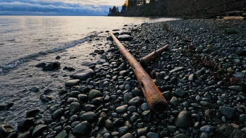 Slow motion waves as camera tilts up on a rocky beach at sunrise Stock Footage 129657137