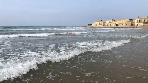 Slow motion of waves crashing on beach w/ stone buildings in the background. Video stock 113640364
