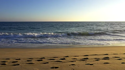 Slow motion of waves hitting a golden beach with footprints in the sand Stock Footage 266440912