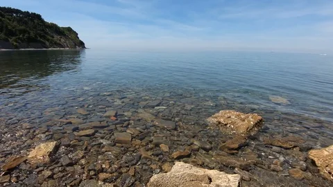 Slow motion waves hitting rocky shore on bright sunny day Stock Footage 130073676
