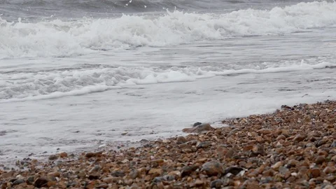 Slow motion waves on pebble beach - handheld. UK, cloudy. Stockbeeldmateriaal 95809371