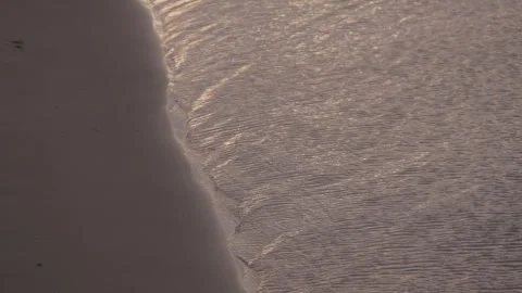 Slow motion of waves rolling onto beach shoreline in soft golden hour light Stock Footage 313298962