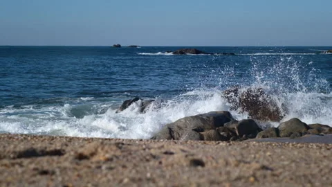 Slow motion waves splashing against rocks on sandy beach, throwing white spray Stock Footage 145710728