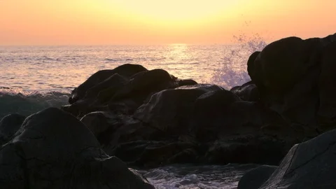 Slow motion waves splashing over rocks on beach at sunset, backlit Stock Footage 115996029
