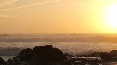 Slow motion waves splashing on rocks on beach at sunset with sun behind Stock Footage 116755054