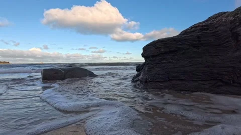 Slow motion waves wash around beach boulders low angle under blue sky Stock Footage 325720840