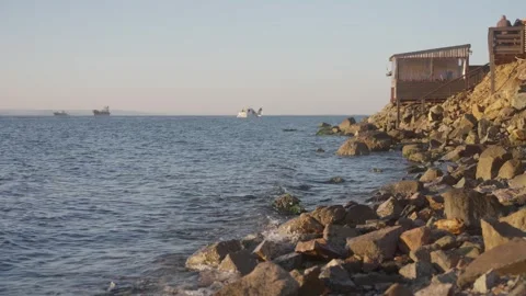 Slow Motion of Waves Washing Rocky Shore Beside Seaside Wooden Cabin at Dusk in Stock Footage 344232296