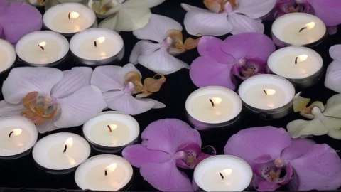Slow motion of waving candle flames, floating among orchid flowers on dark water Stock Footage 99851421