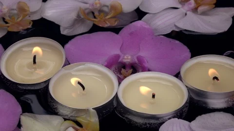 Slow motion of waving candle flames, floating among orchid flowers on dark water Video stock 99852178