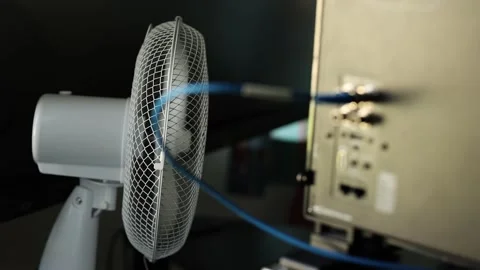 Slow motion of a white desk fan blowing air near computer monitors and Stock Footage 341954121