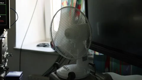 Slow motion of a white desk fan blowing air near computer monitors and Stock Footage 341954209