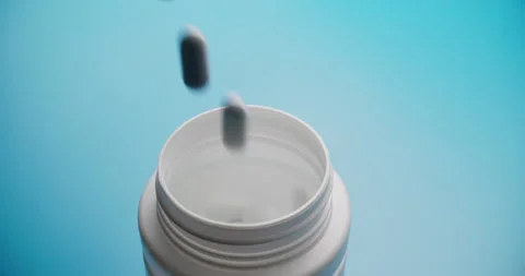 Slow motion white pill bottle with falling tablets on blue Stock Footage 307949127
