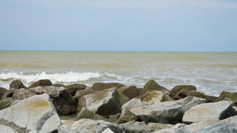 A slow-motion wide shot of waves crashing onto the rocks at the beach Stock Footage 231763359