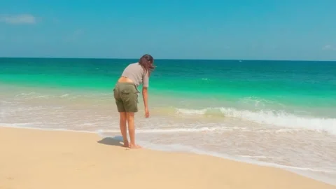 Slow motion of woman bending down touching sea water on tropical sandy beach Stock Footage 345391931