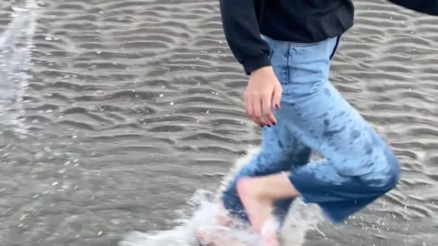 Slow motion of woman running barefoot in water on the beach and splashing water Stock Footage