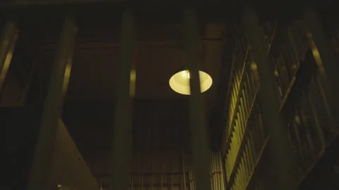 Slow motion of yellow light bulb lighting up a cell in prison during night time Stock Footage 208751309