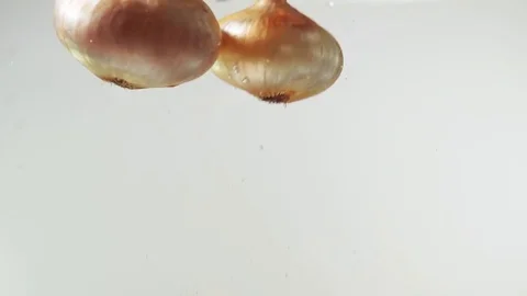 Slow motion: yellow onion falling into water, white background Stock Footage 84744373