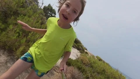 Slow motion of a young boy running through rocky terrain near the sea, wearing a Stock Footage 313842945