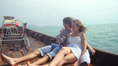 Slow motion of young couple sitting at deck on drifting wooden boat enjoying Stock Footage 87944402