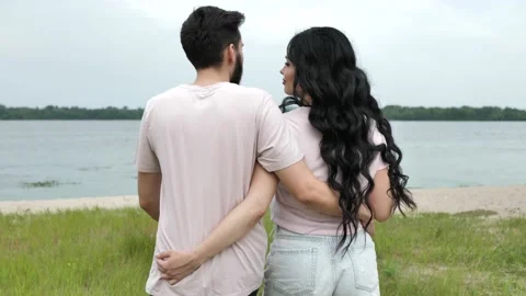 Slow motion, a young couple walks along the river bank, hugging their waists and Stock Footage 205004486