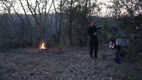 Slow motion young man alone in the forest by the fire looks for the flashlight Stock Footage 274738815