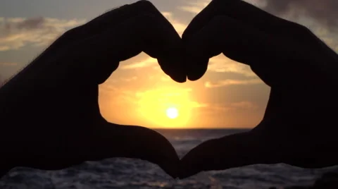 SLOW MOTION: Young man capturing beautiful golden sun with heart shaped hands Stock Footage 64278203