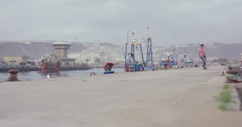 Slow motion of young man driving on skateboard through harbour with docked boats Stock Footage 158646774