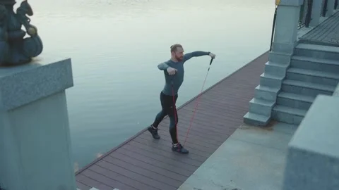 Slow motion young man exercising with trx suspension strap near lake crossfit Stock Footage 138654151