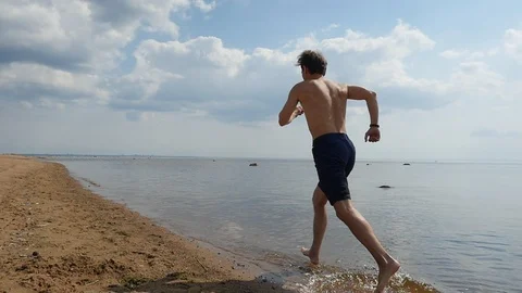 Slow motion of young man jogging shirtless on sandy beach, Rear view Video stock 93411210