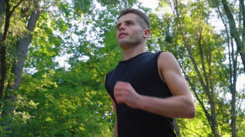 Slow motion young man jogging under green trees Stock Footage 158319009