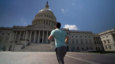Slow motion of young man running close to the US Capitol and turning to look at Stock Footage 128717886