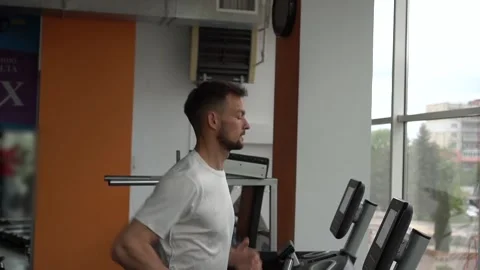 Slow motion of a young man running on treadmill in fitness center. Side view. Stock Footage 132171953