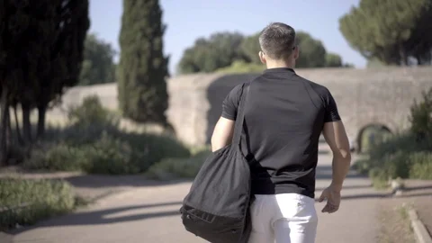 Slow motion: A young man strolling around the park with a black sports bag on Stock-Footage 90887966